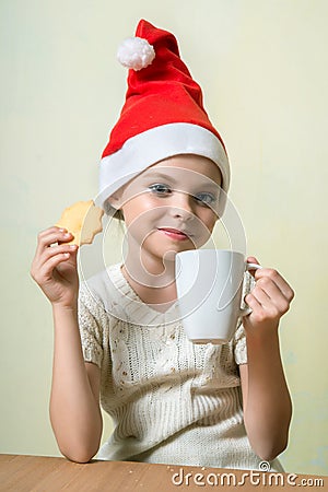 Ð¡ute girl in Santa Claus hat eat cookies. Stock Photo